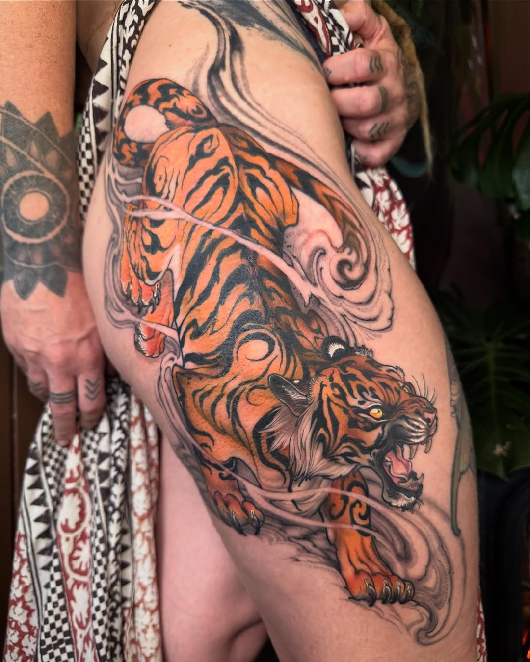 Orange and black tiger tattoo with decorative swirls covering the thigh and hip area, featuring a detailed tiger head with yellow eyes.