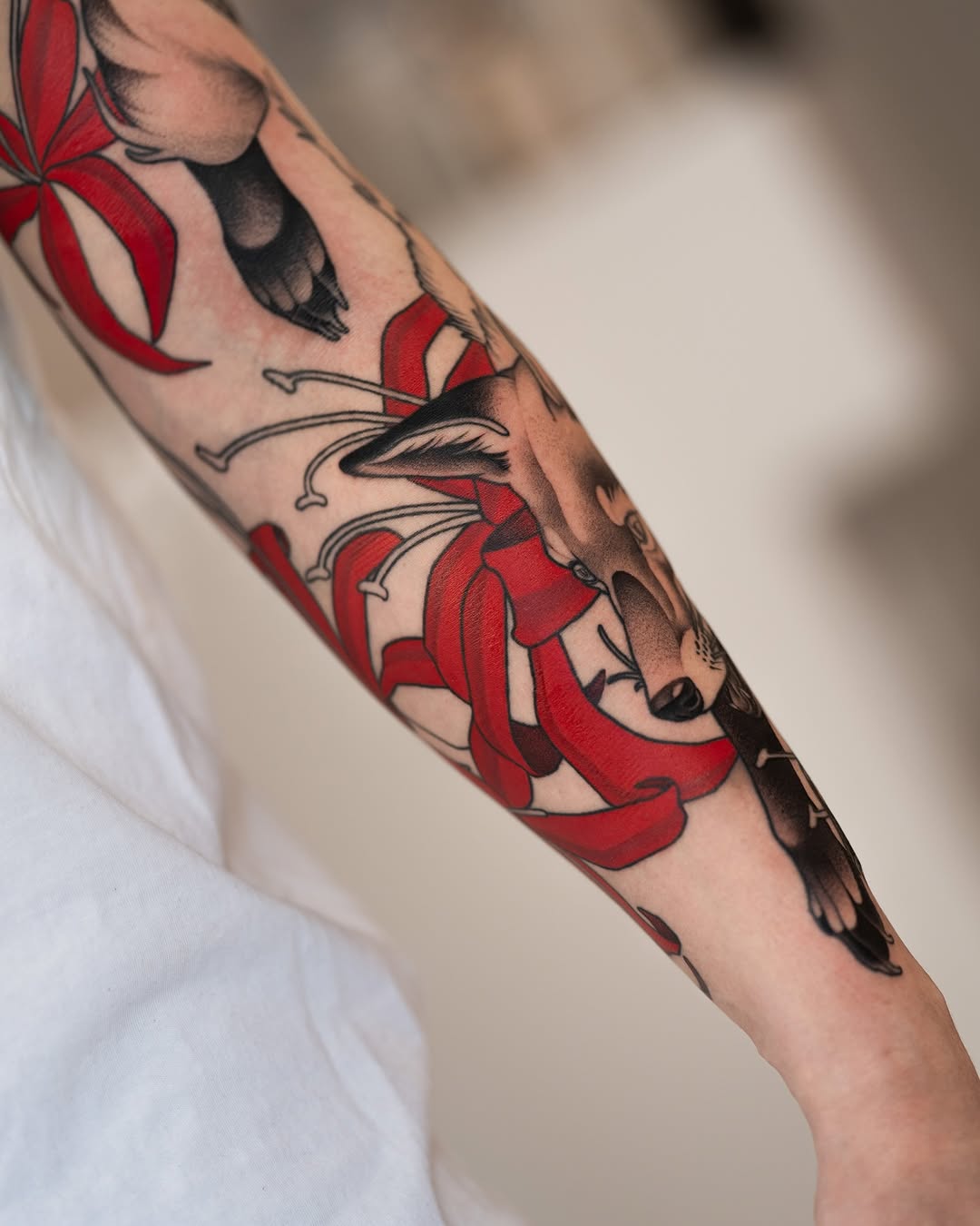 Colorful tattoo sleeve featuring red flowers and black birds on an arm, displayed against a white background.
