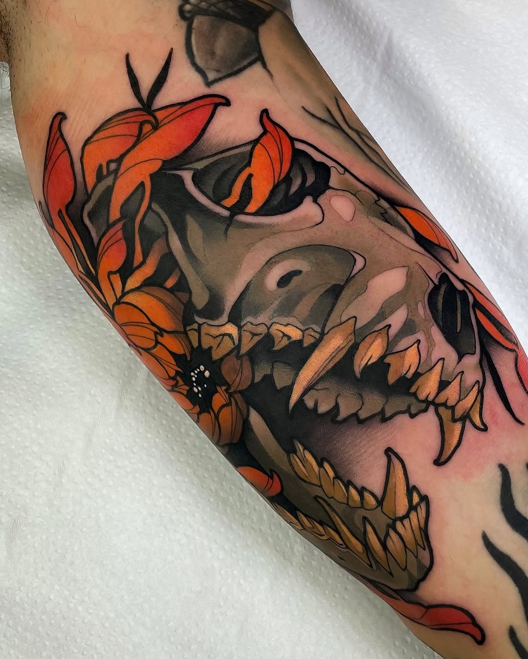 Colorful skull tattoo on forearm featuring orange and red flowers, black shading, and detailed teeth work displayed on skin.