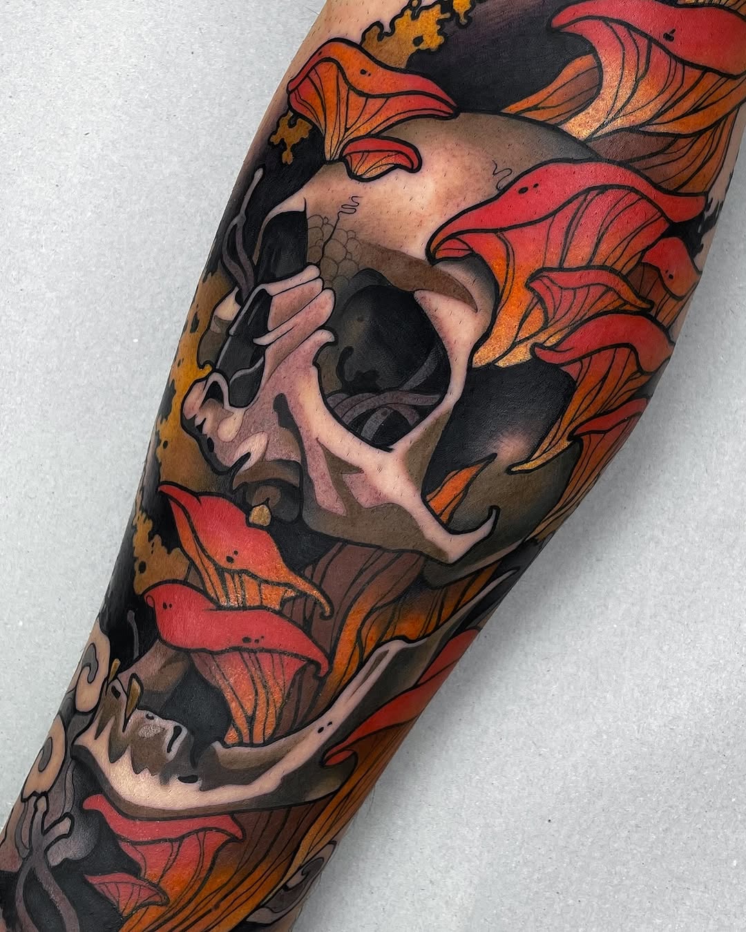 Skull with red and orange floral wings on forearm, featuring tan and black shading with detailed linework.