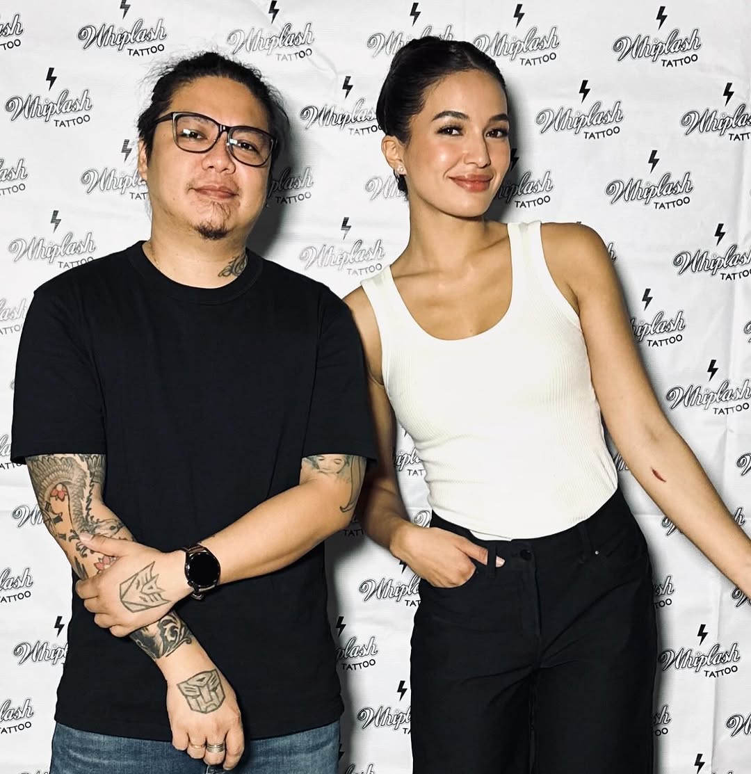 Two people at a tattoo studio event display various tattoos on their arms and hands in black ink.