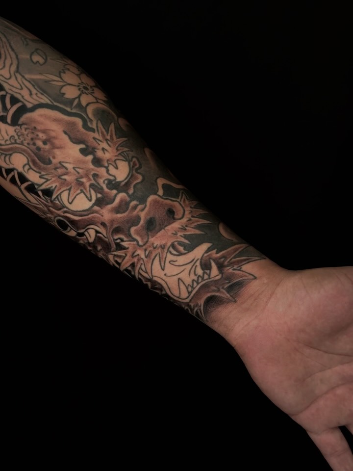 Detailed arm sleeve tattoo featuring ornate floral and botanical motifs in black and gray ink covering the forearm and wrist area.