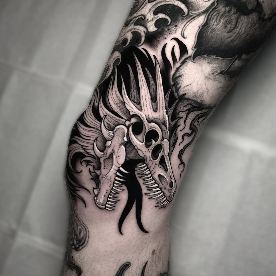 Detailed black ink tattoo of an ornate dragon head with scrolling flourishes and anatomical details on the upper arm and shoulder.