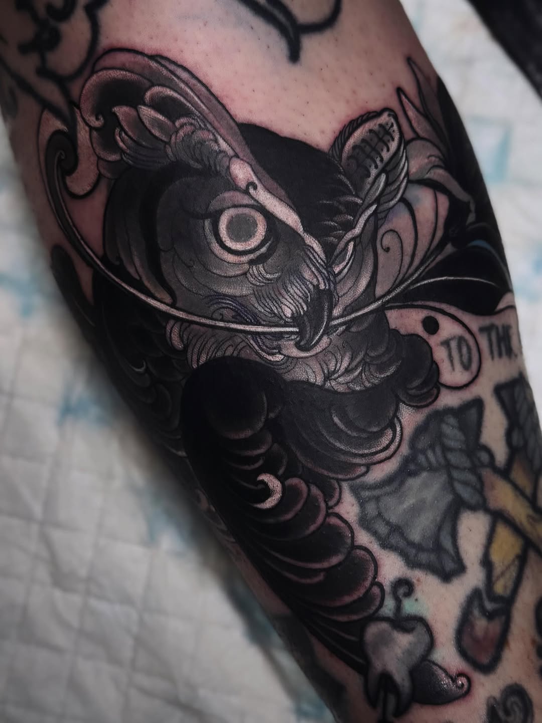 Ornate owl tattoo with decorative scrollwork and flourishes in black and grey ink on the upper arm and shoulder.