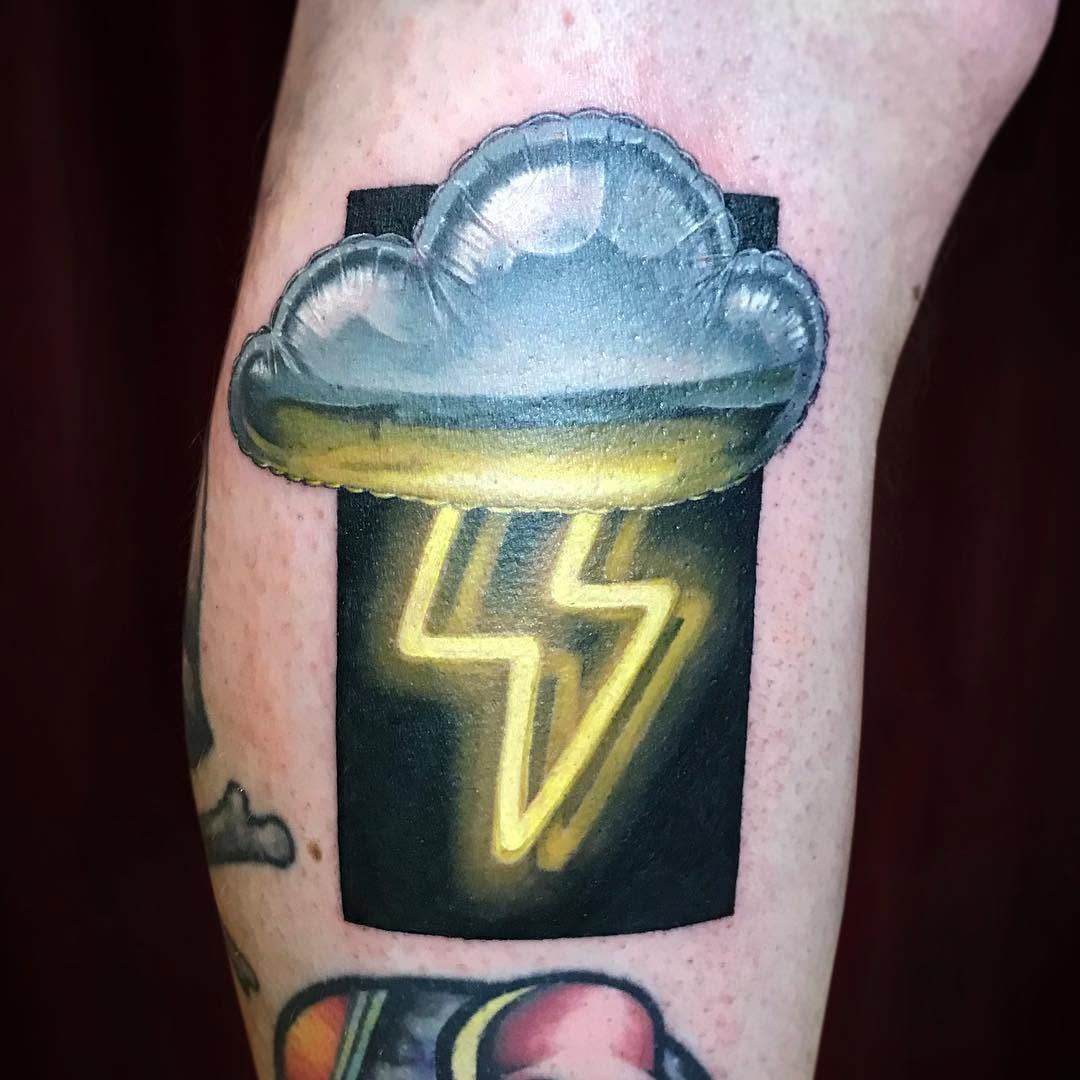 Cloud-topped container with glowing yellow lightning bolt symbol tattooed on calf, featuring blue, yellow, and black colors.