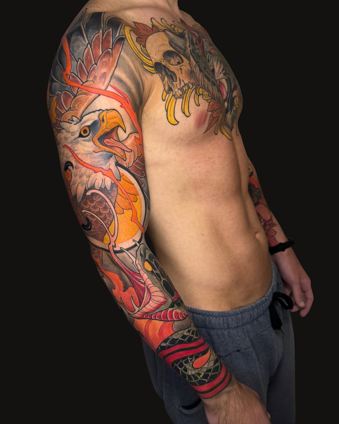 Full-sleeve arm tattoo featuring an eagle, skull with bananas, fish, and ornamental red linework in orange, yellow, and red tones.