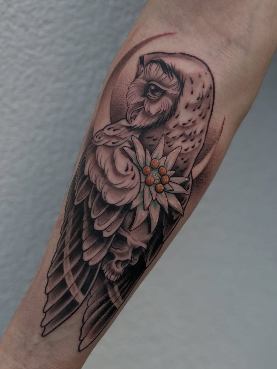 An owl with detailed feathers and a flower tucked near its wing in black and orange ink on a person's forearm.