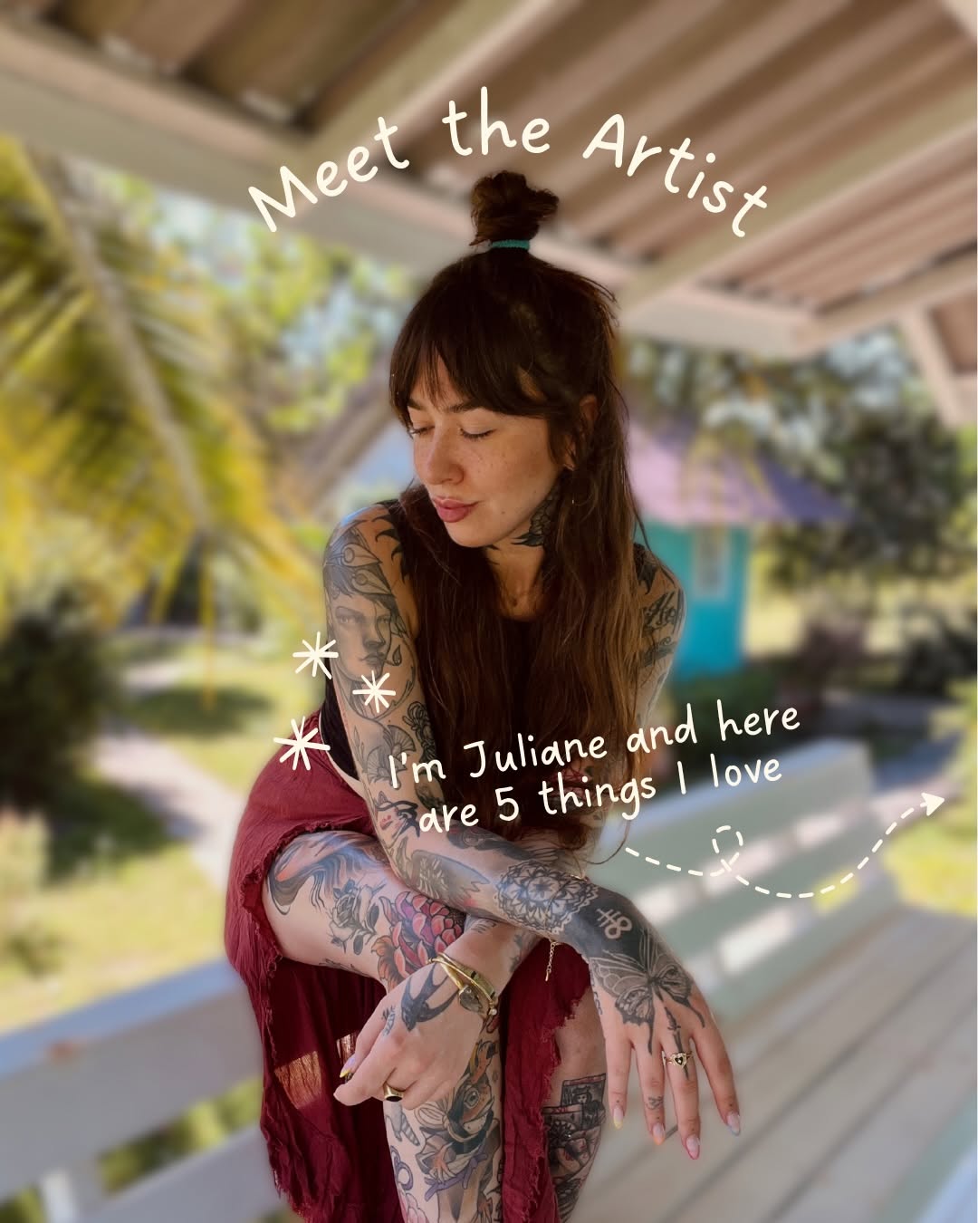 Tattooed woman with extensive arm and leg tattoos in black and colored ink featuring various designs, wearing a burgundy wrap in an outdoor garden setting.