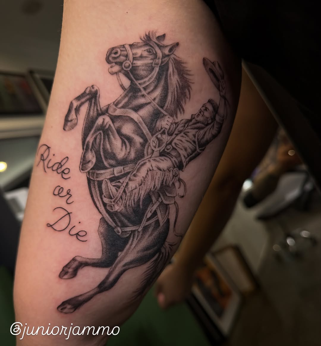 Rearing horse with saddle and rider in grayscale ink on upper arm, accompanied by cursive text reading "Ride or Die.