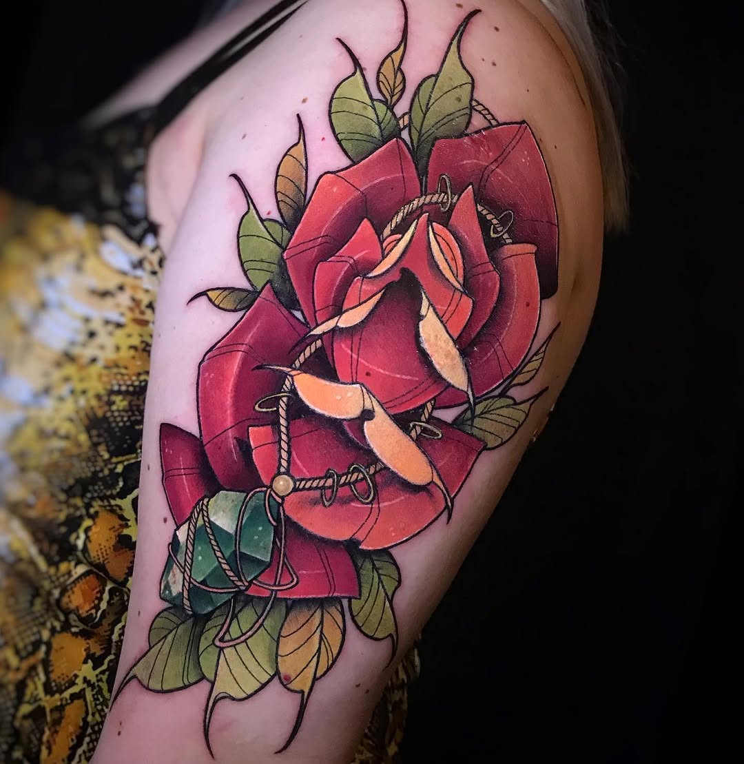Red rose with green leaves and rope details wrapped around the petals, tattooed on the upper arm in red, orange, green, and teal colors.