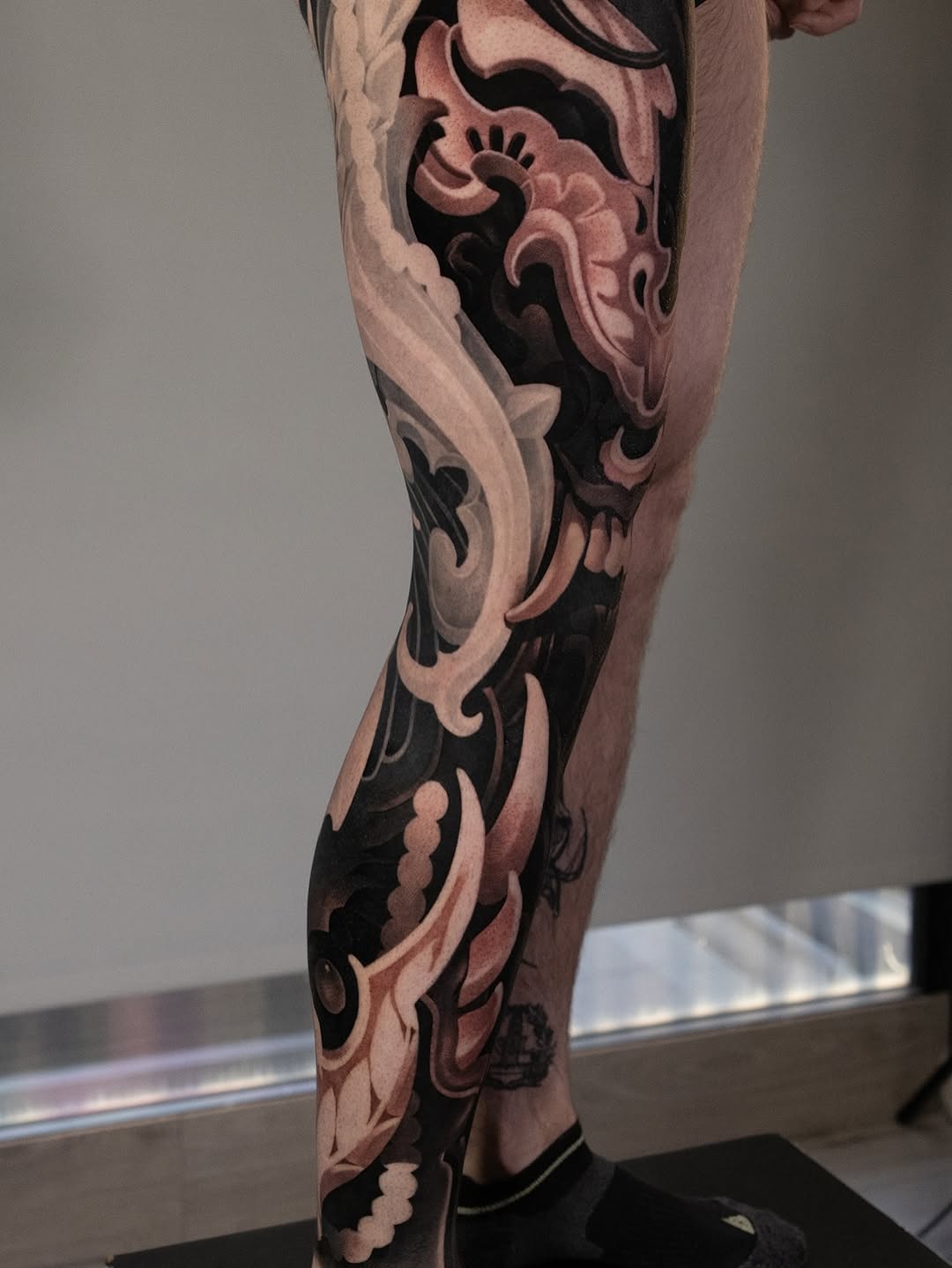 Full leg tattoo featuring ornate baroque scrollwork and flourishes in black and pink tones on the thigh and calf.