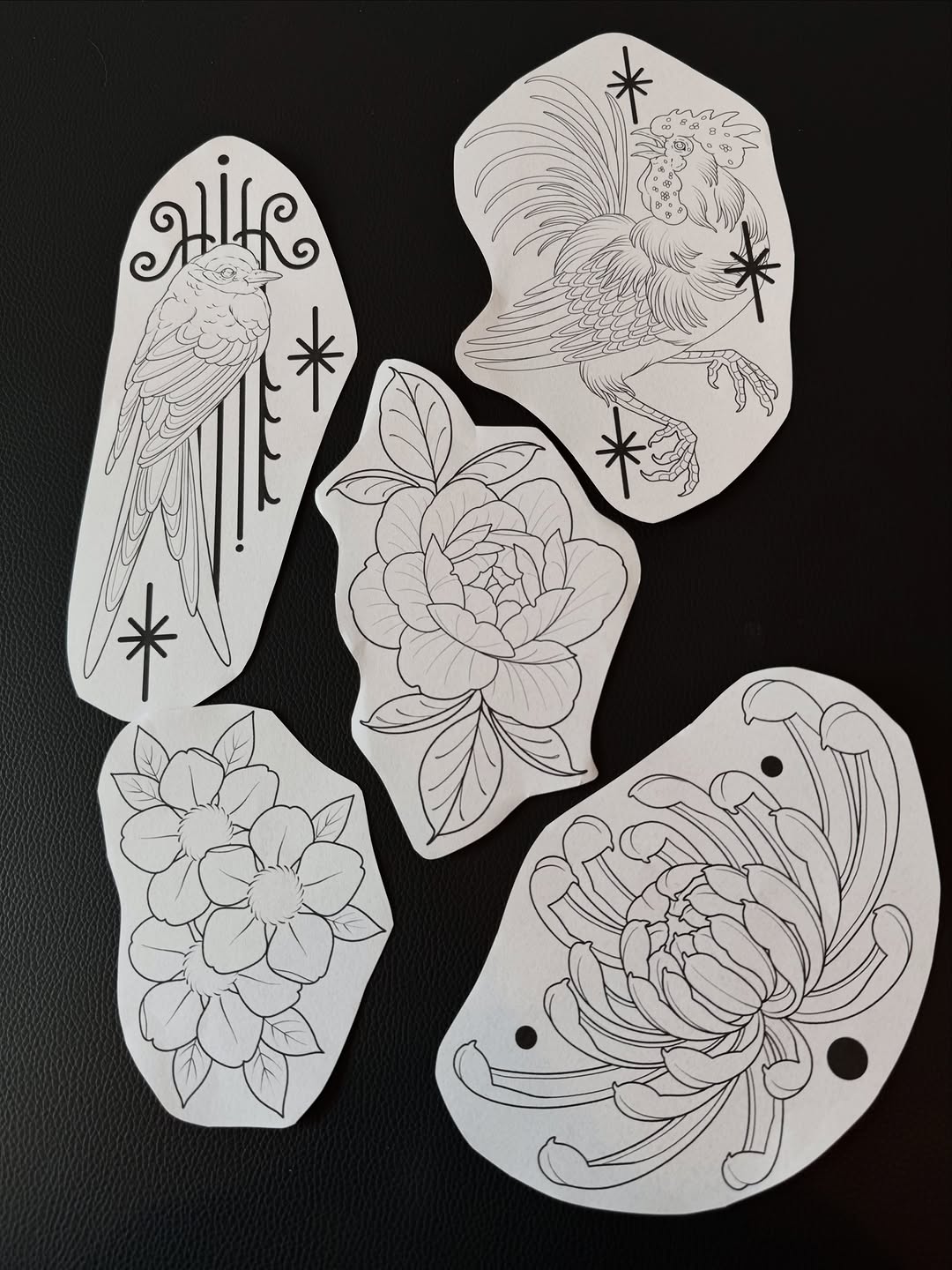 Five white stencil templates featuring line-drawn birds, flowers, and celestial symbols arranged on black background for tattoo design reference.