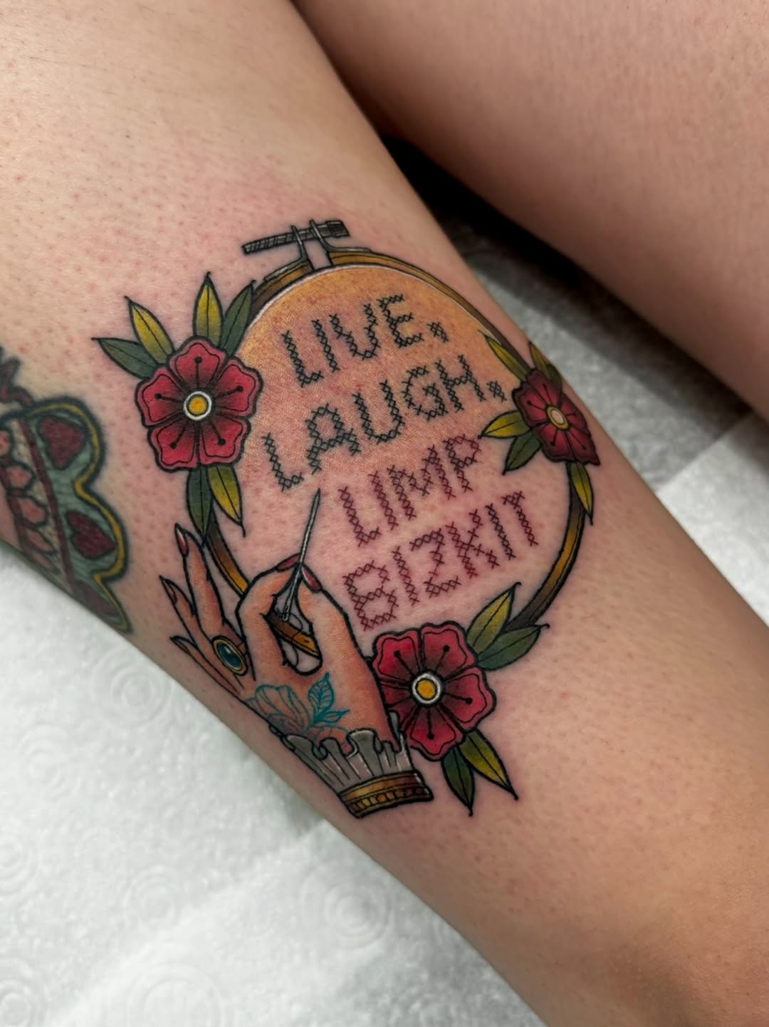 Hot air balloon tattoo with red flowers, green leaves, scissors, and text reading "live laugh love" on upper arm in color.