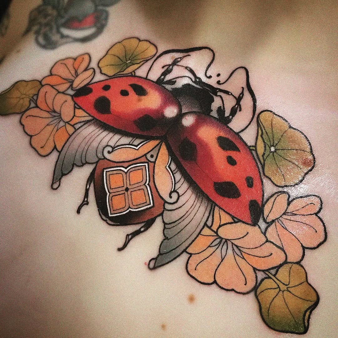Colorful ladybug tattoo with red wing covers and black spots, surrounded by orange and yellow flowers on pale skin.
