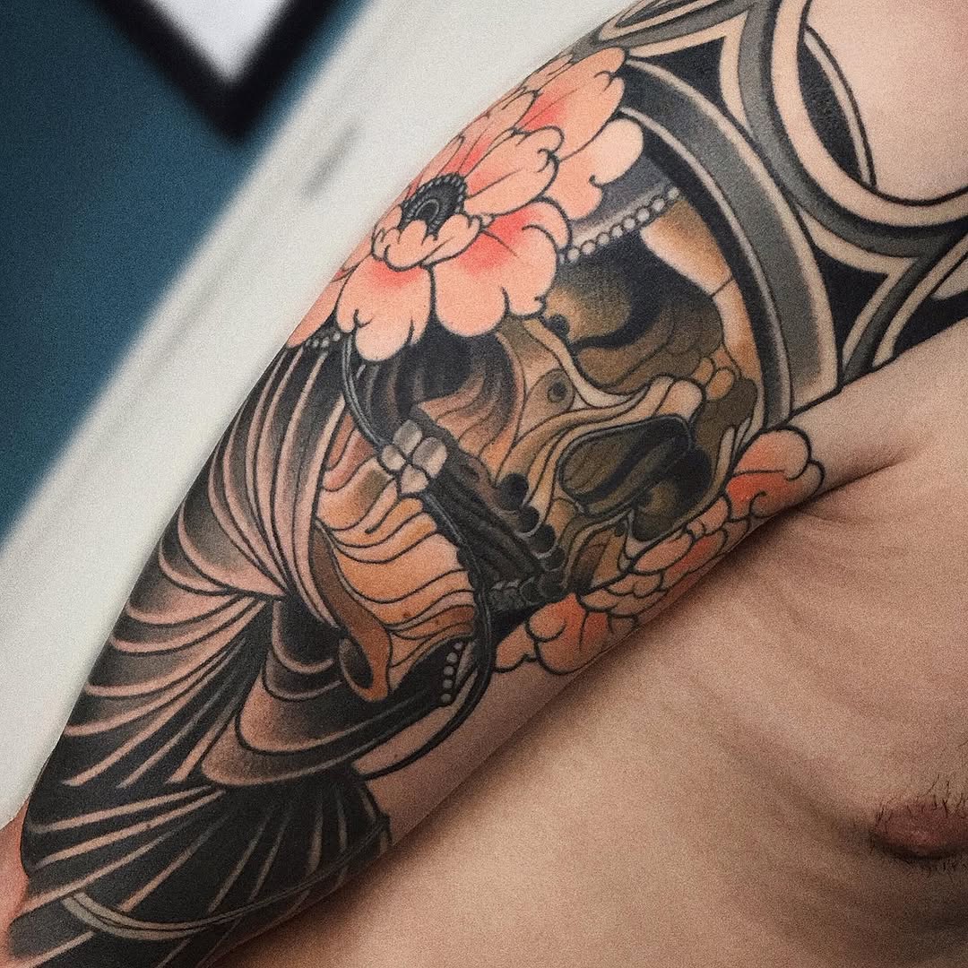Colorful arm tattoo featuring a winged figure with coral and black tones, ornate details, and decorative elements wrapped around the upper arm and shoulder.