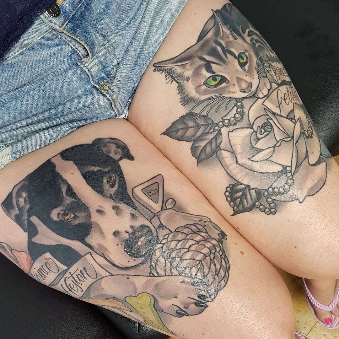 Two animal portrait tattoos on thighs featuring a cat with green eyes and a dog with amber eyes, each surrounded by decorative floral and ornamental elements in black and gray ink.