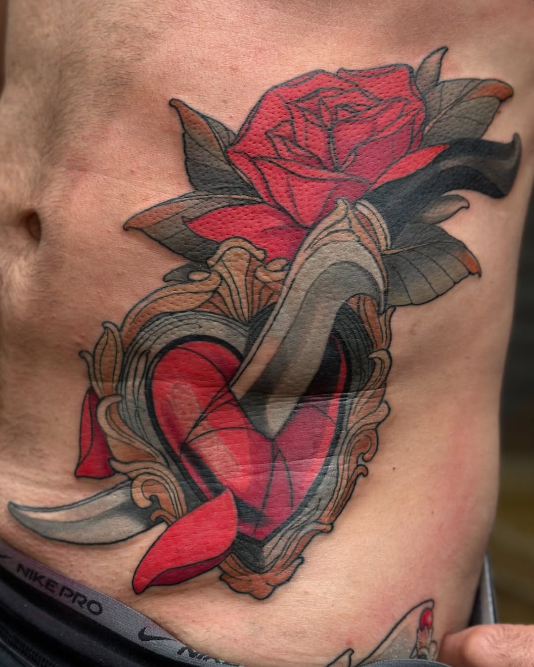 Red rose with green leaves and an ornate gray banner frame on a man's chest, featuring detailed shading and gold accents.