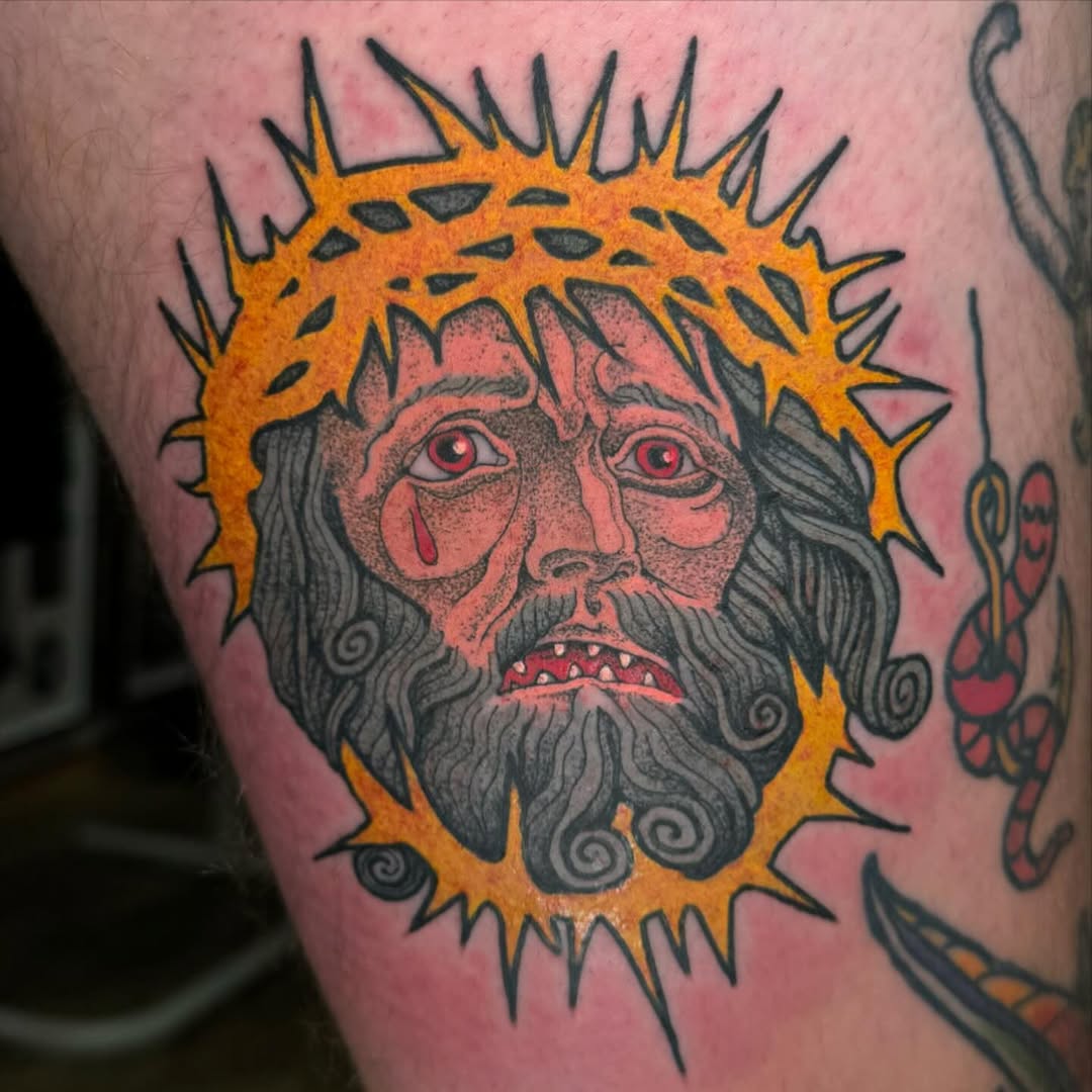Bearded face with red eyes and spiked orange halo on upper arm, featuring gray hair, red mouth, and decorative spiral details.