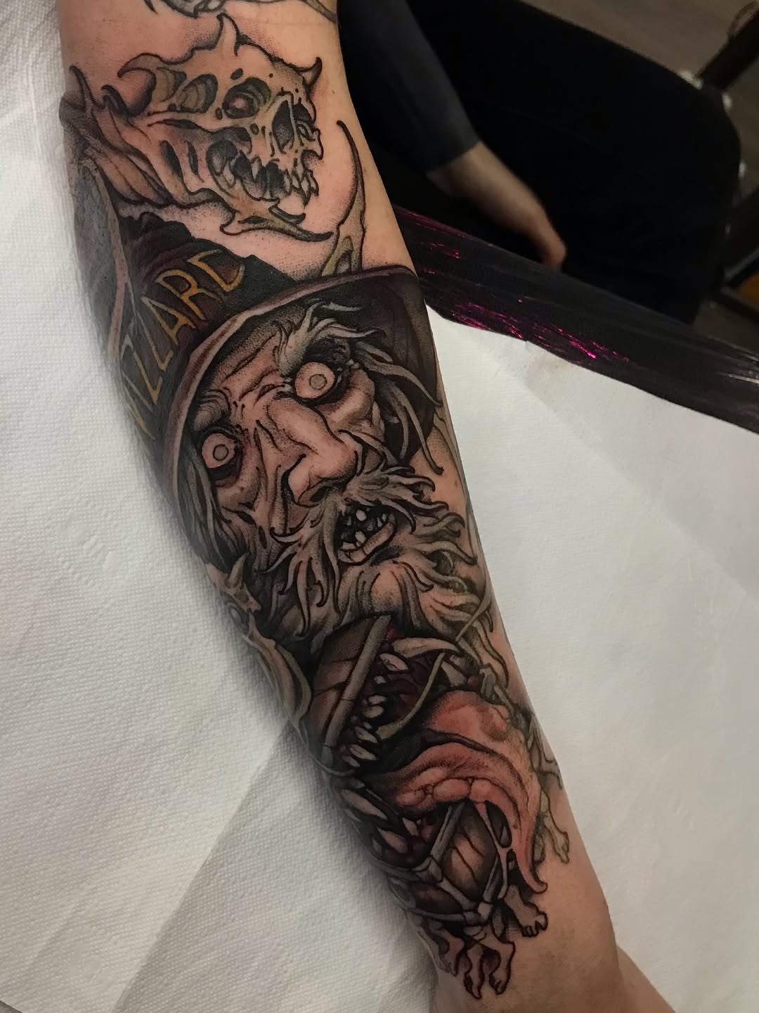 Arm sleeve tattoo featuring stacked demon and skull faces with ornamental details in black and brown ink on tan skin.
