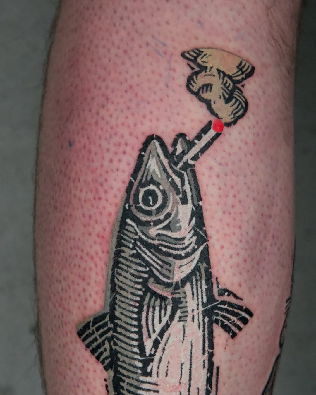 Fish with open mouth holding a red dot on its tail, rendered in black and gray ink on calf.