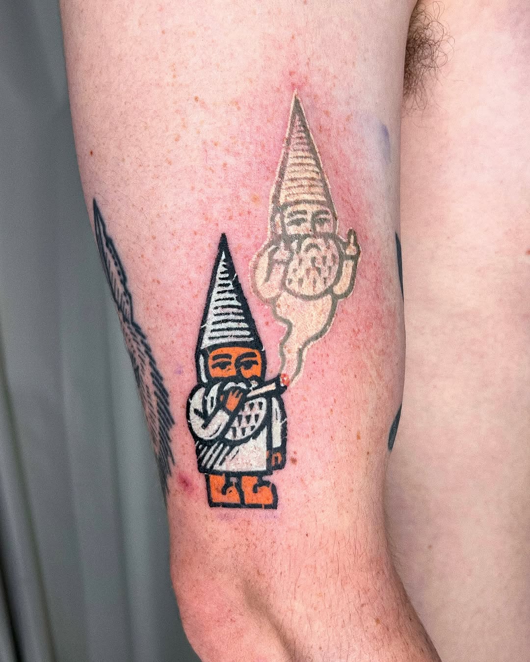 Colorful gnome tattoo with pointed hat, orange accents, and smaller gnome figure above on upper thigh.