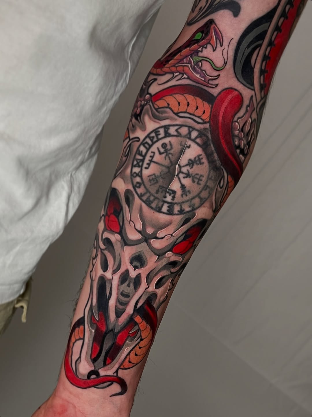 Full-color arm sleeve tattoo featuring a demon head, anatomical skull, serpent, compass circle, and red heart design.
