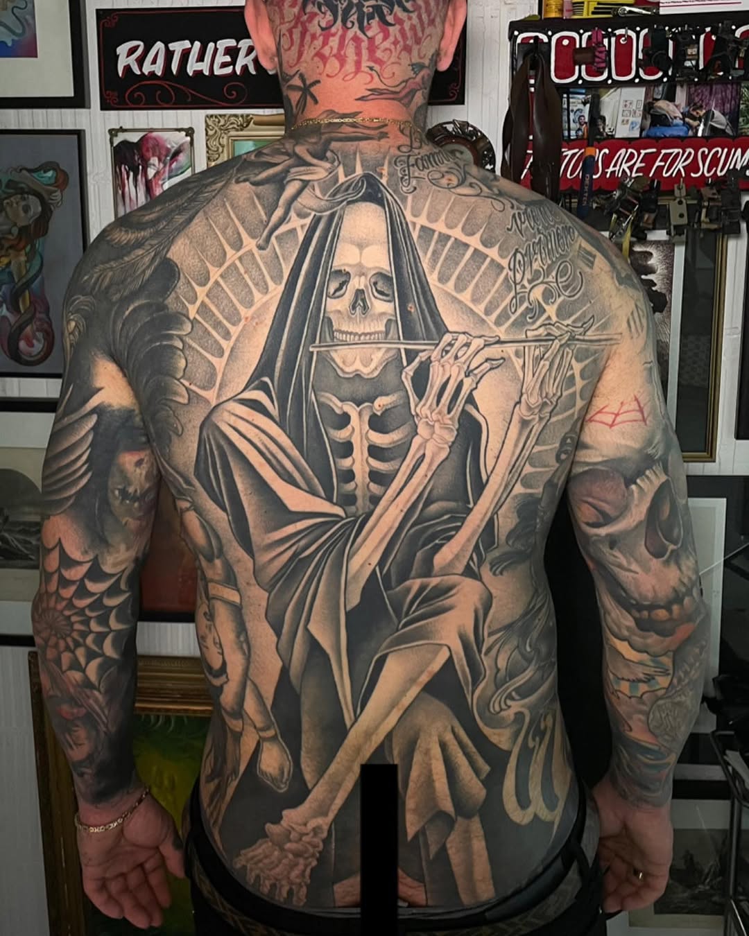 Back tattoo featuring a skeletal figure in robes holding a scythe, surrounded by skull imagery and decorative elements in black and grey ink.