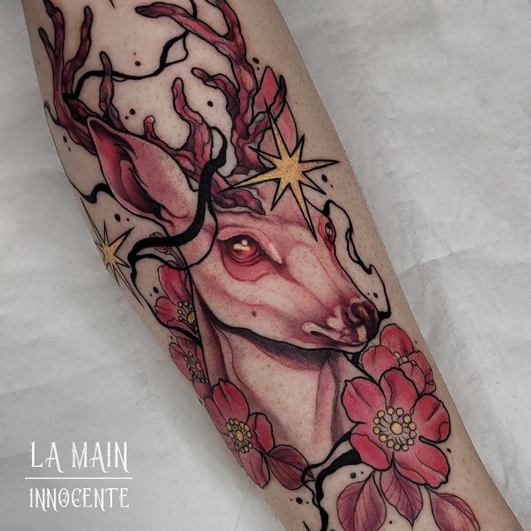 Colorful deer head tattoo with branching antlers, golden stars, and red flowers on the forearm, featuring a glowing eye detail.