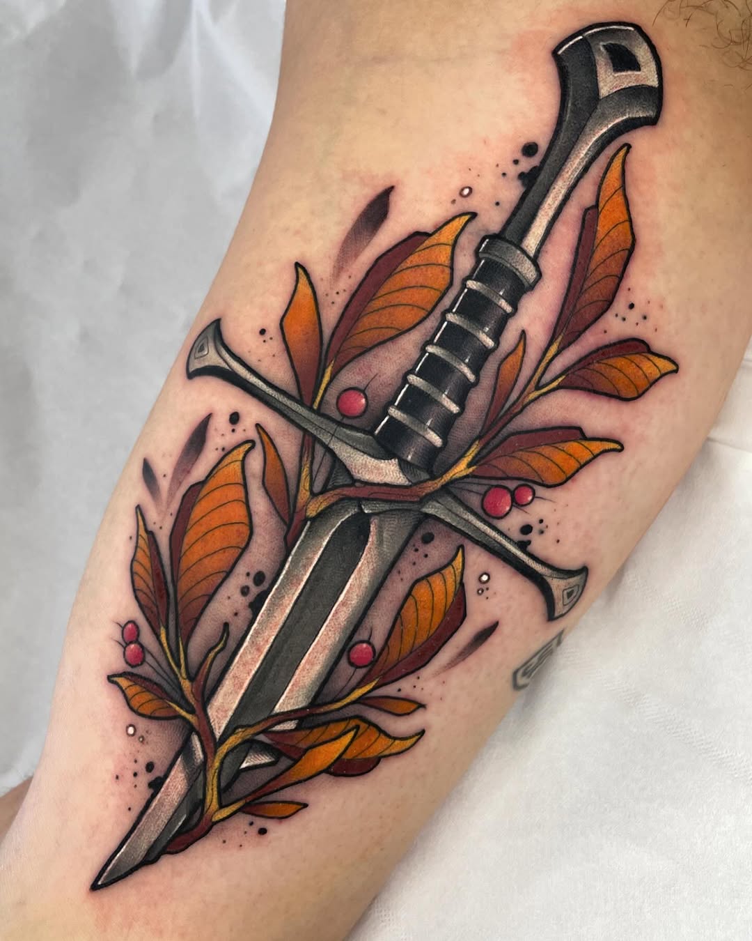 Wrench and adjustable tool with orange and burgundy autumn leaves and red berries wrapped around the blade, tattooed on an arm.