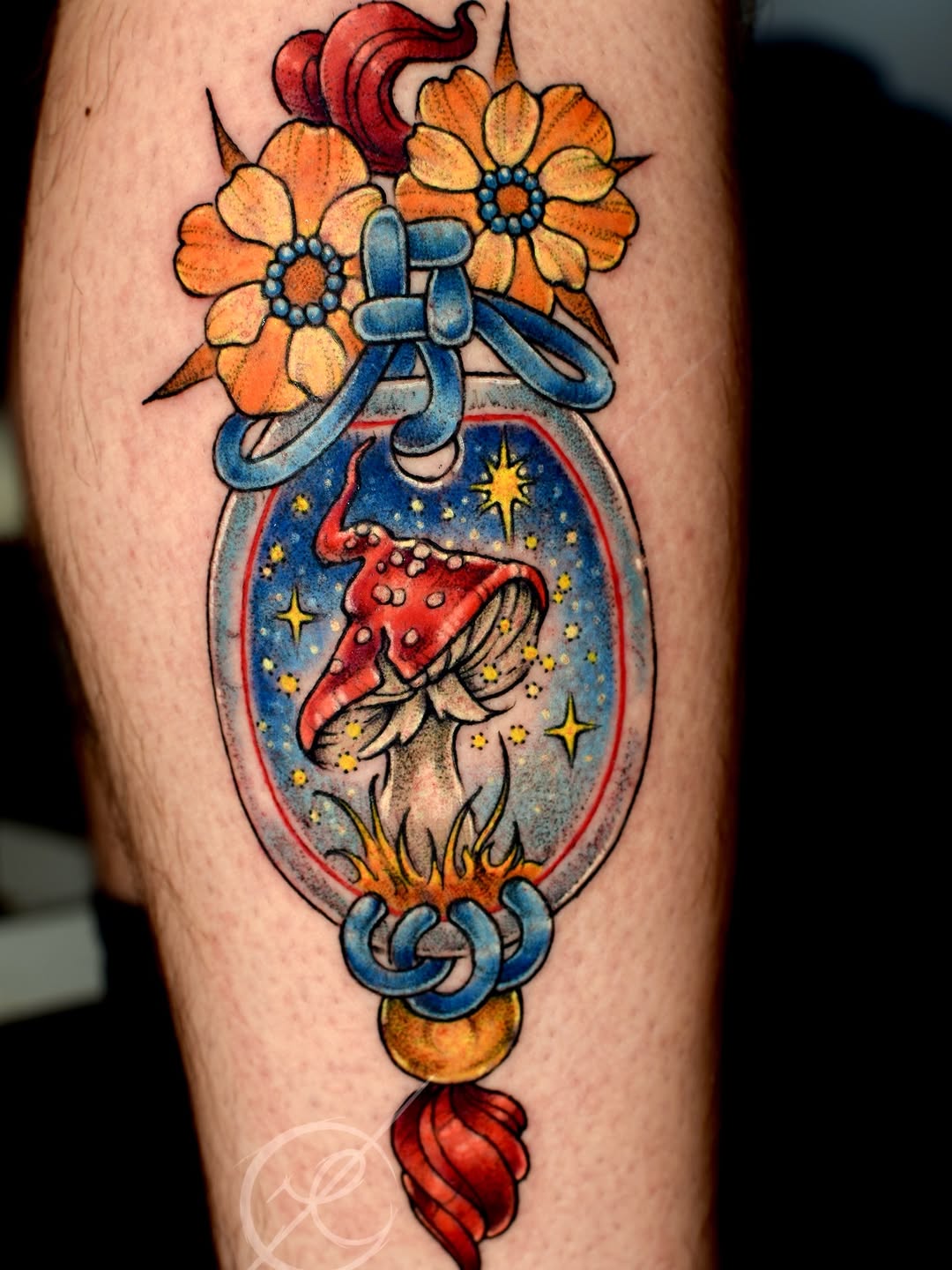 Colorful tattoo on leg featuring a glass globe with a red mushroom and stars inside, topped with orange flowers and a blue ribbon.