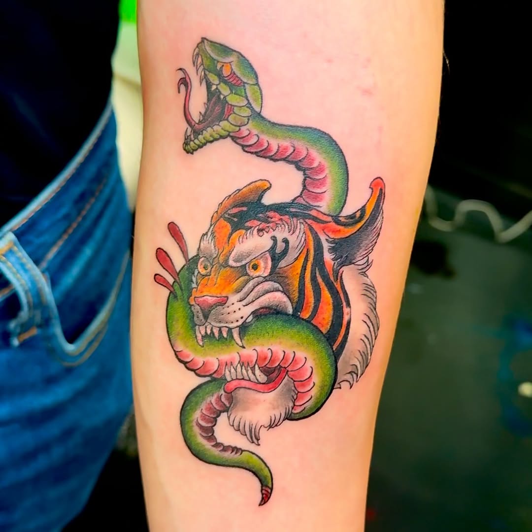 Colorful arm tattoo featuring a green serpent coiled around a tiger's head with orange, pink, and black markings.