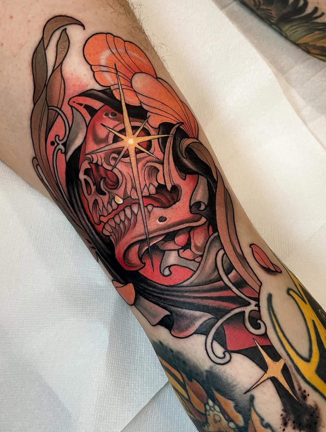 Red and black skull with ornate swirls and golden stars on the forearm, featuring detailed shading and decorative flourishes.