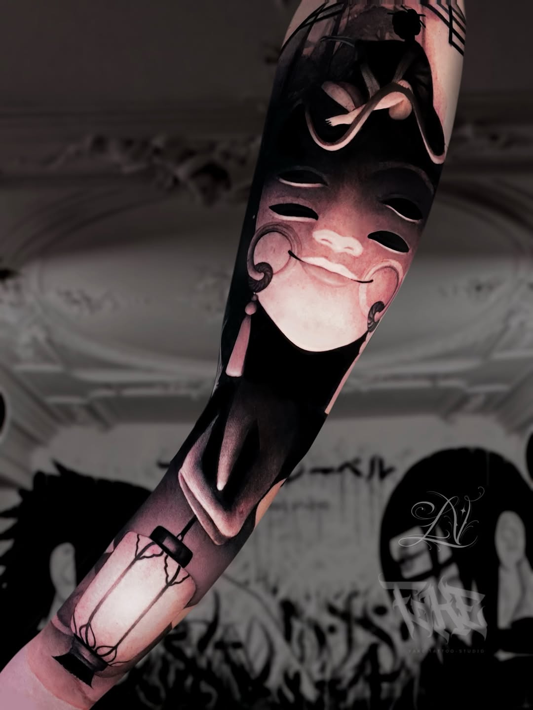 Arm tattoo featuring stacked theatrical masks with ornate details in pink and black shading, displayed on a pale forearm against a dark background.