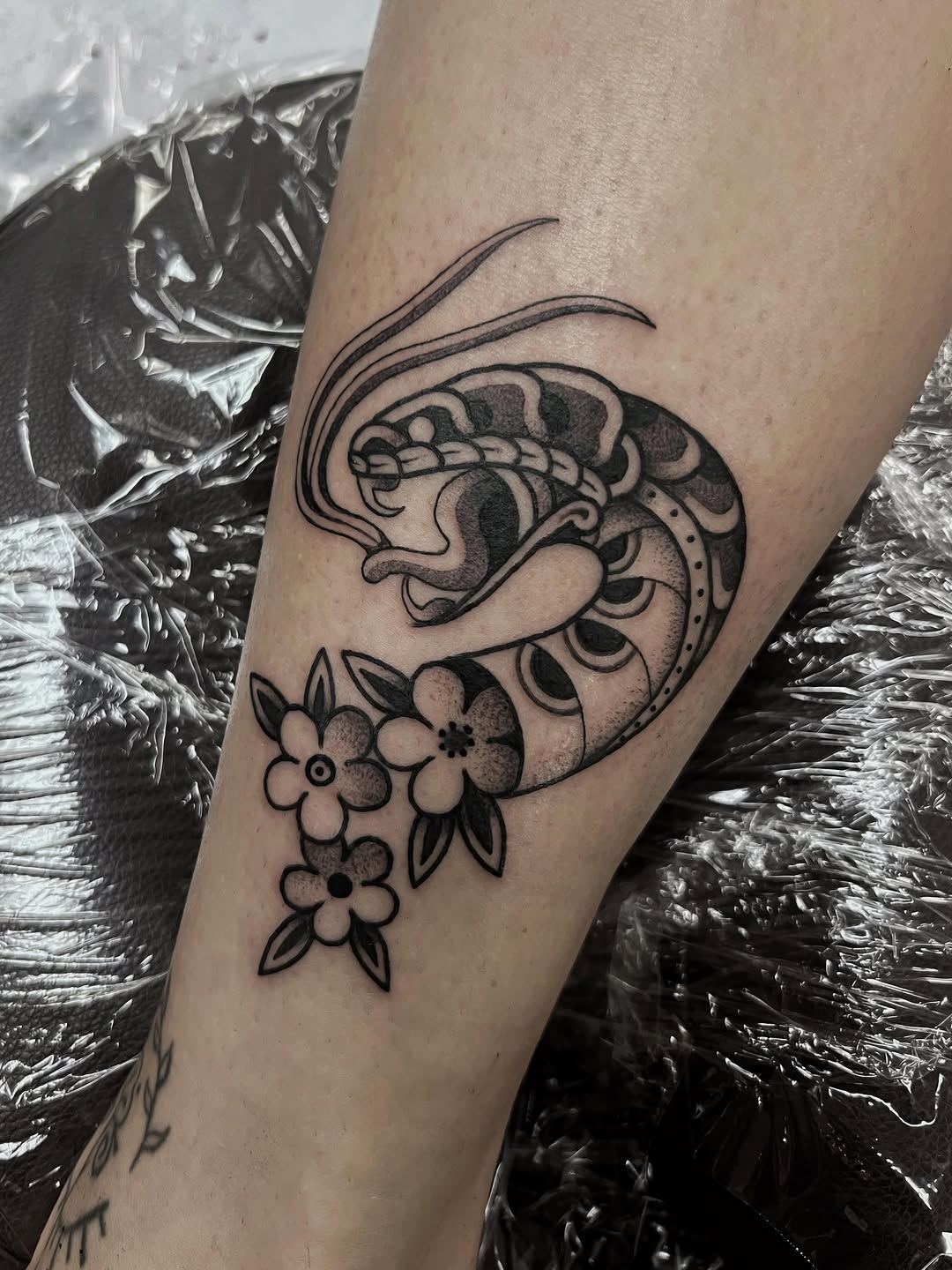 Decorative dragon with curled horns and scaled details paired with small flowers on the forearm, rendered in black ink with gray shading.