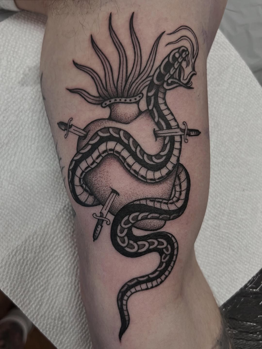 Dragon wrapped around two ornamental spheres with swords piercing through, featuring detailed scales and a crowned head, tattooed on the calf in black ink.