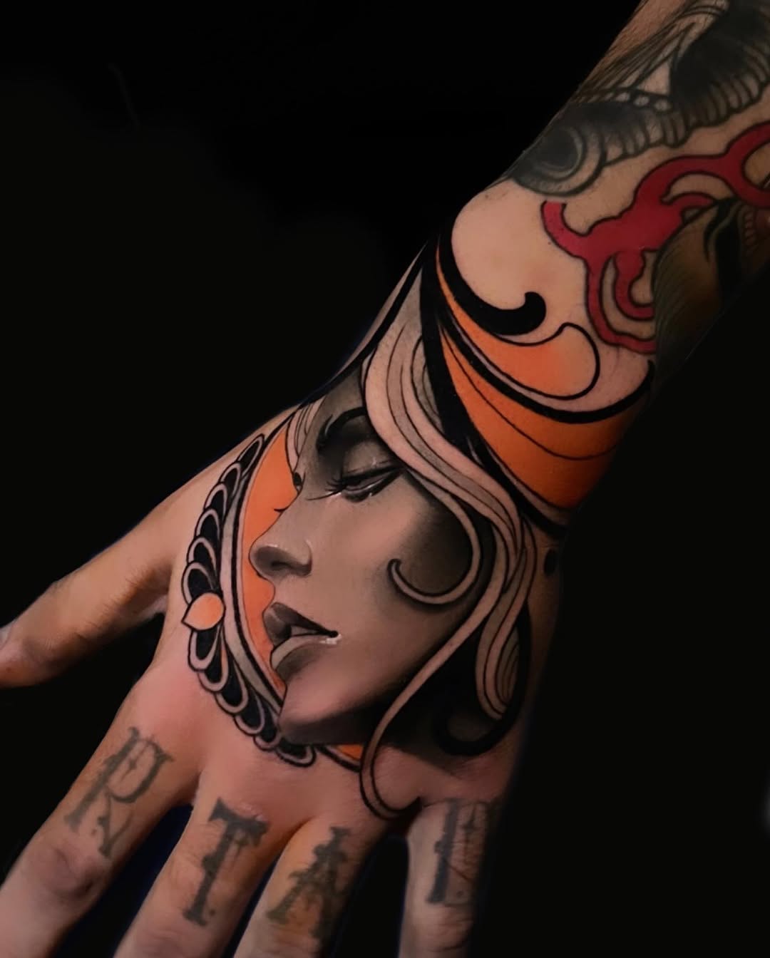 Female portrait tattoo on hand and forearm featuring orange and red tones with decorative elements and text on fingers.