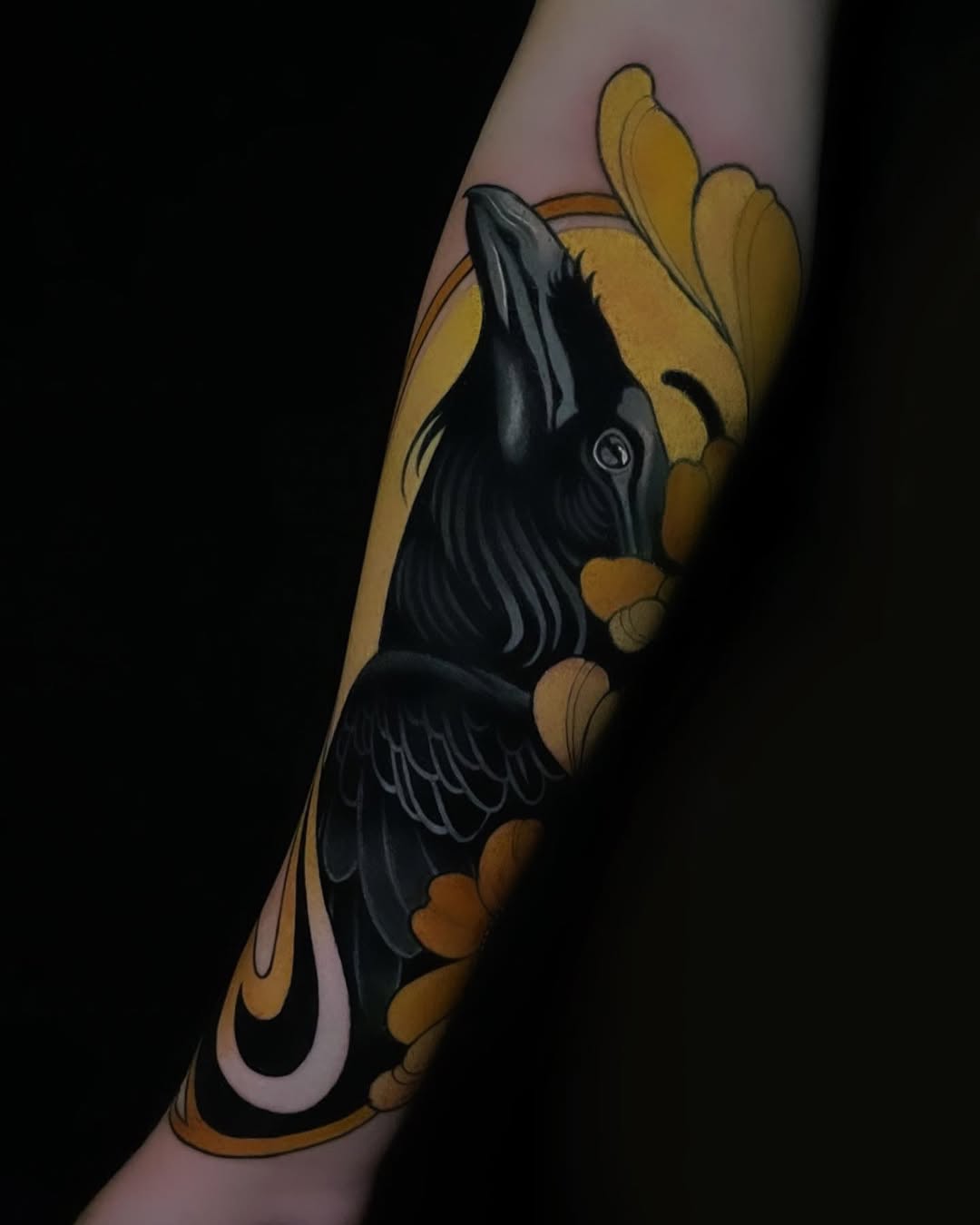 Black raven with wings spread perched on a golden yellow hand against a pale background, tattooed on the forearm.