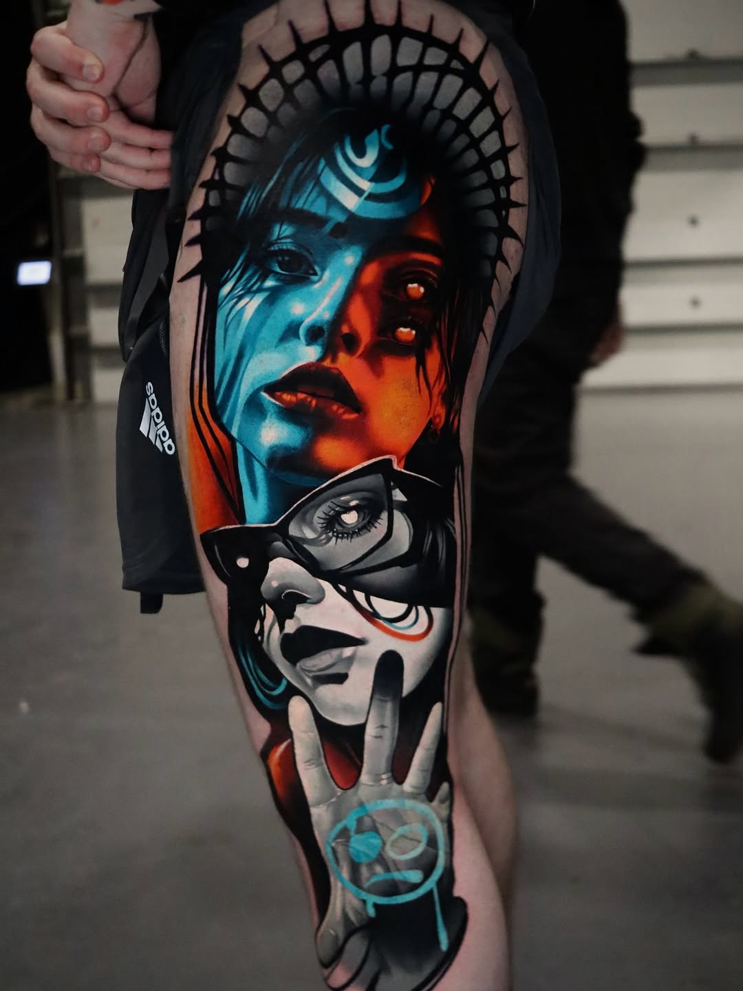 Two stylized female faces with geometric patterns in turquoise and red tones on the upper arm and forearm, featuring sunglasses and decorative line work.