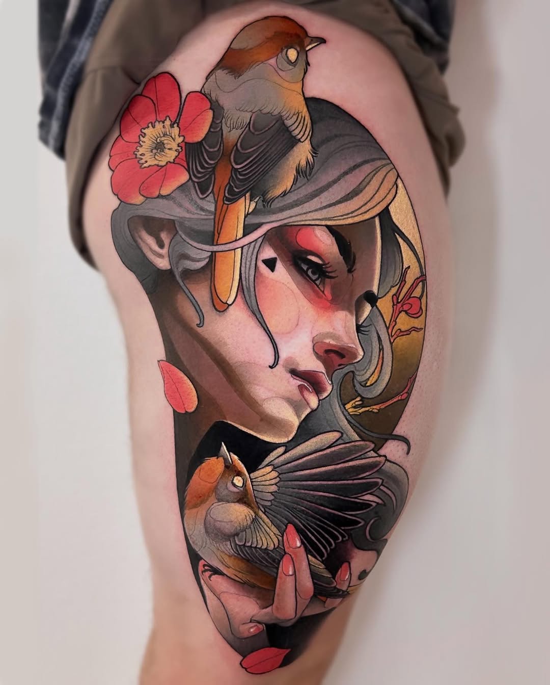 Colorful thigh tattoo featuring a woman's face with birds and red flowers, showcasing detailed shading and vibrant reds, browns, and earth tones.