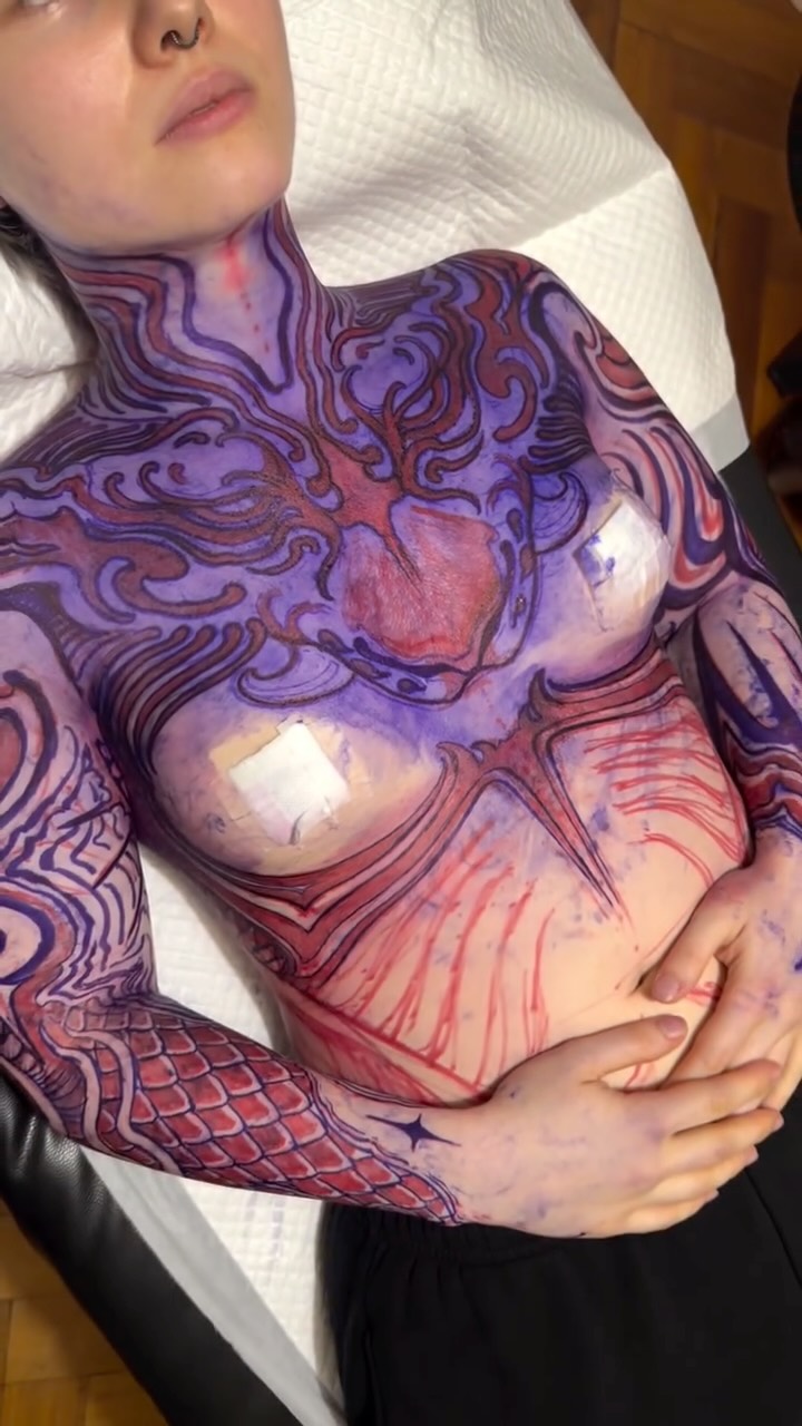 Colorful chest and torso tattoo featuring purple, red, and coral swirling patterns with anatomical heart design and scale details.