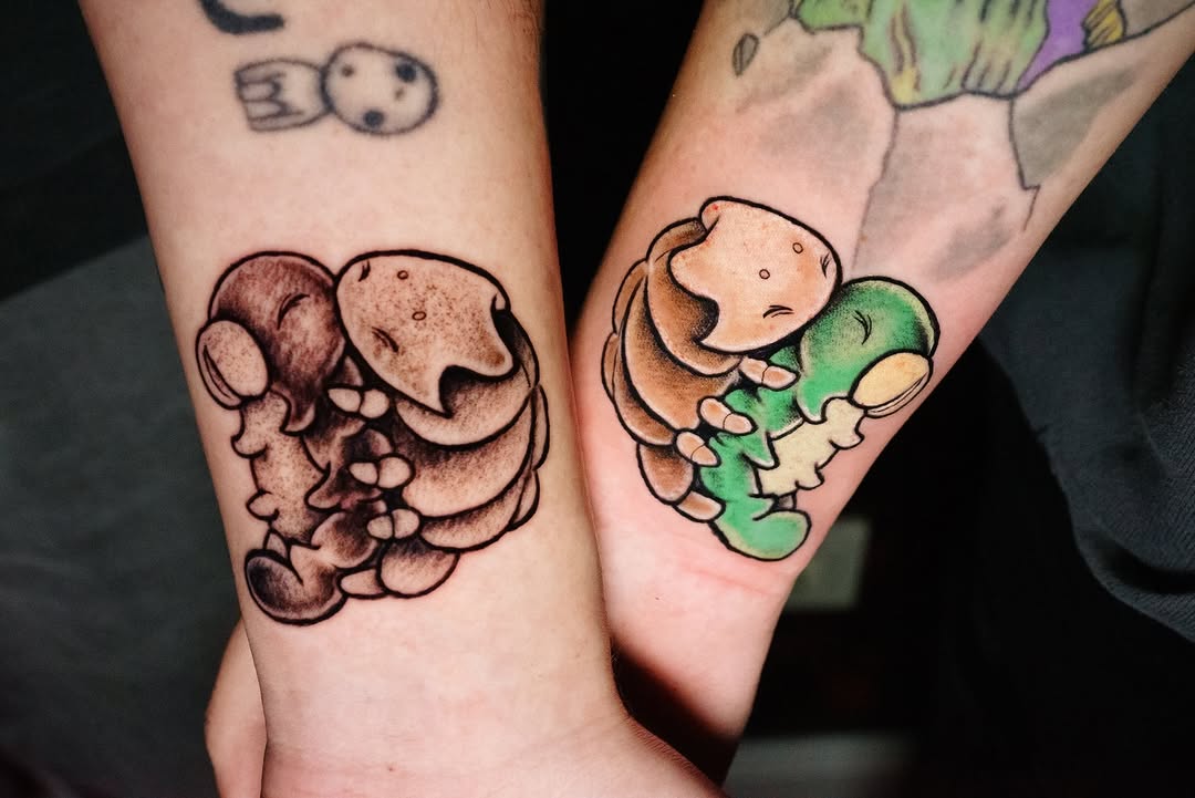 Two matching couple tattoos on inner forearms featuring abstract organic shapes in brown and green with cream details, displayed side-by-side.