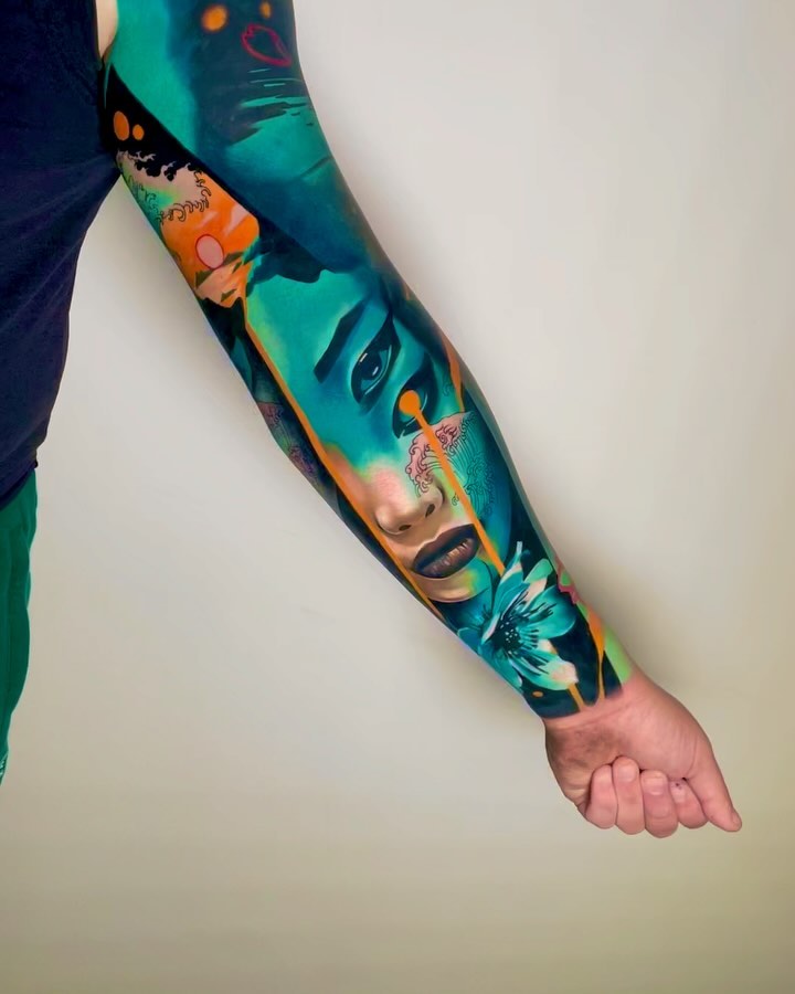 Full-sleeve arm tattoo featuring colorful portraits, eyes, flowers, and abstract elements in teal, orange, and black on a person's forearm and upper arm.