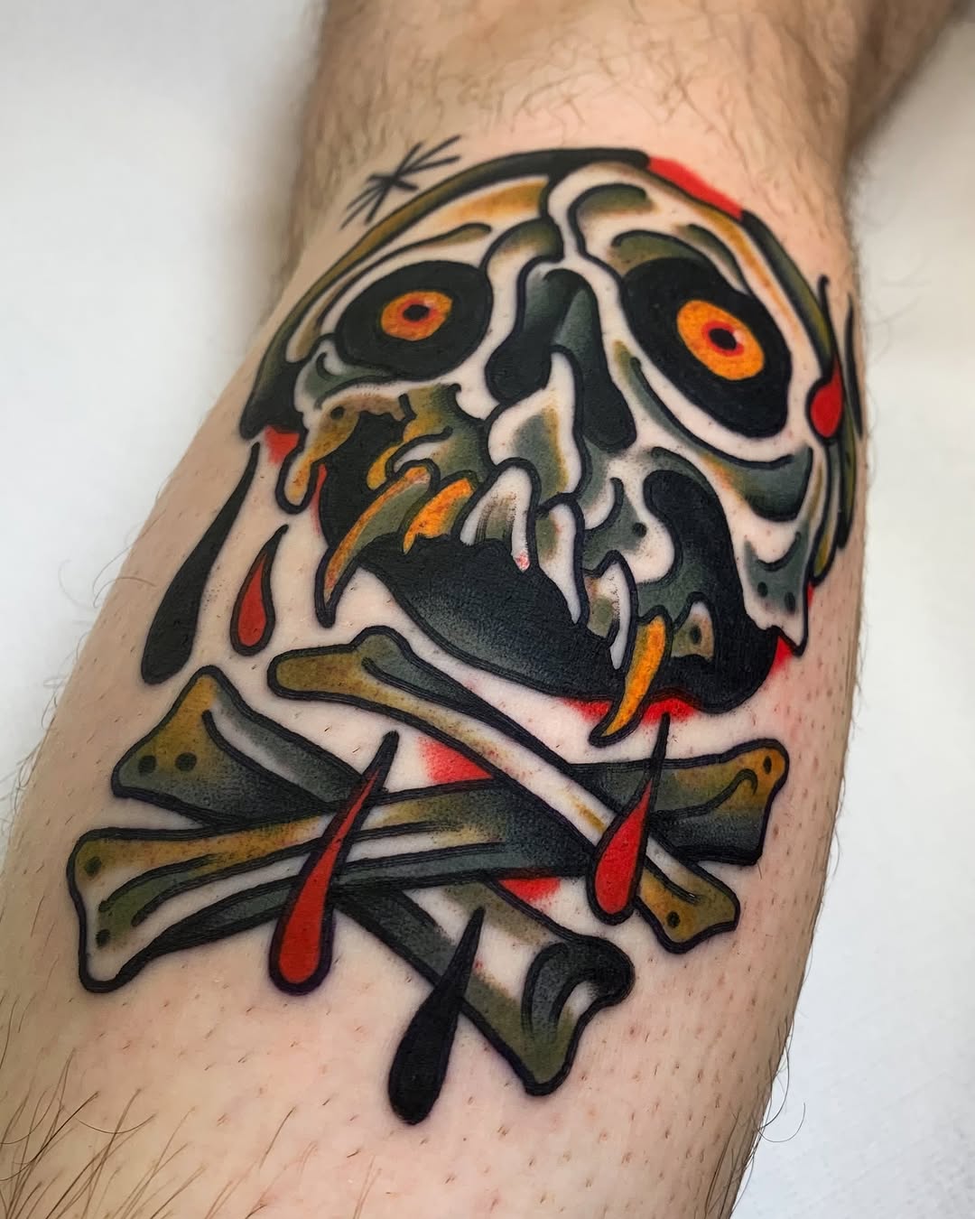 Colorful skull with crossbones tattoo featuring orange eyes, red accents, and black outlines on the forearm.