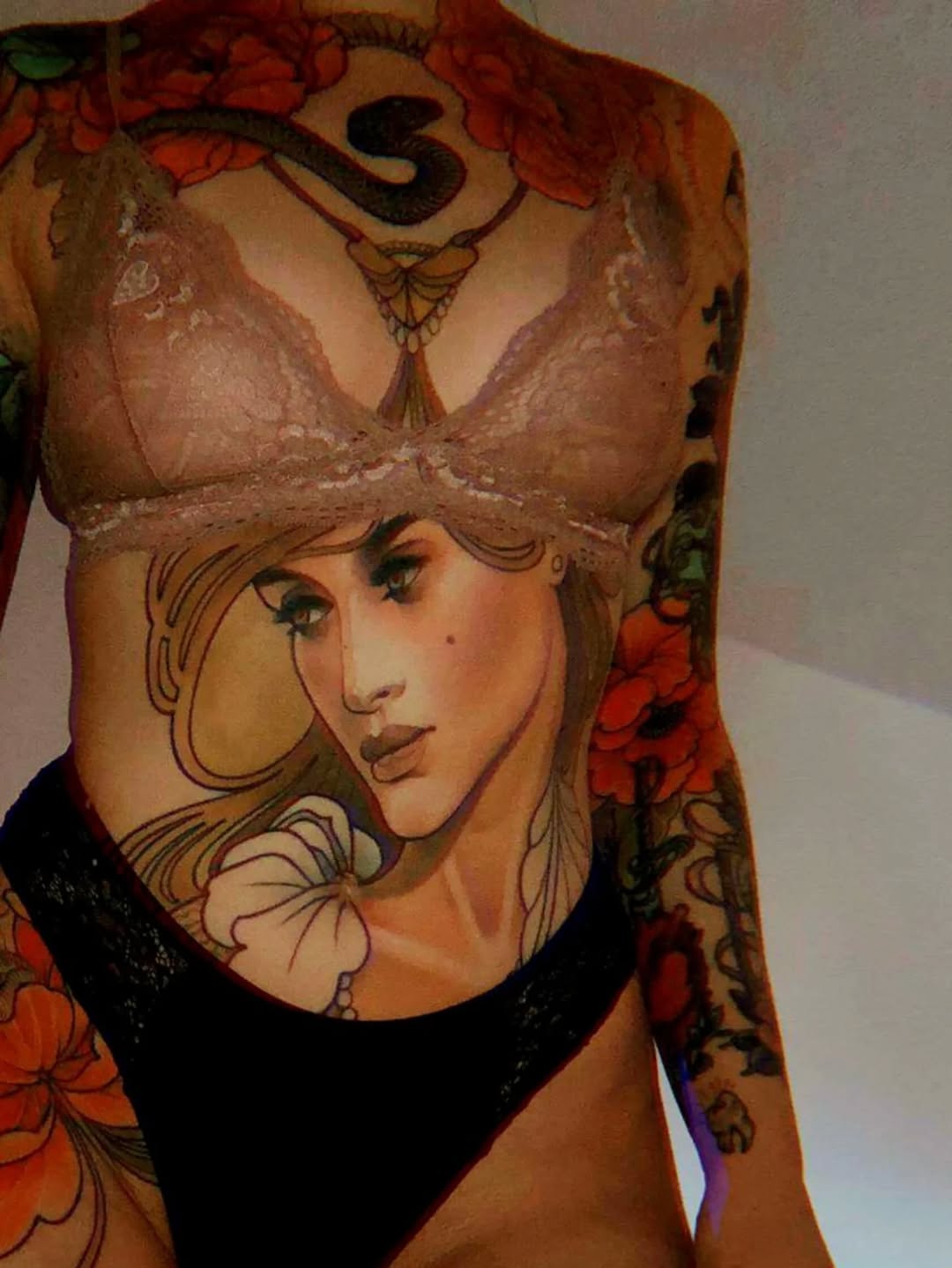 Chest and shoulder tattoo featuring a portrait of a woman's face with flowing hair, surrounded by red and orange flowers, with decorative elements in warm tones.