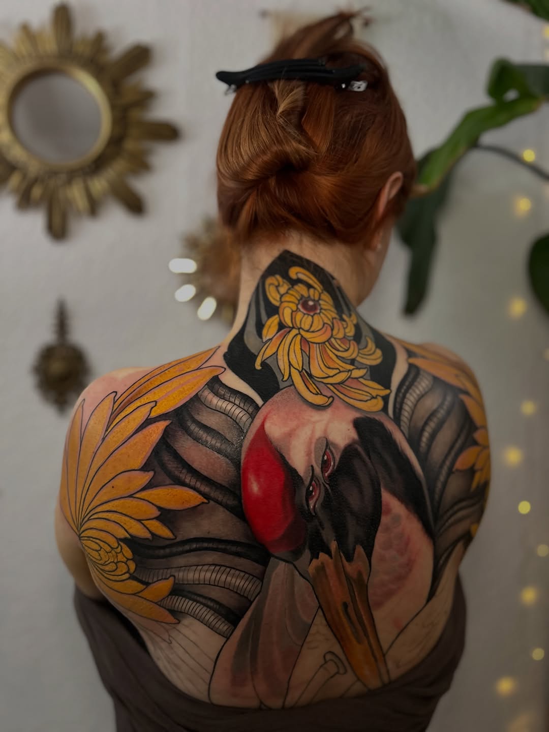 Back tattoo featuring golden sunflowers, red and black bird with wings spread, and decorative line work in yellow, orange, black, and flesh tones.