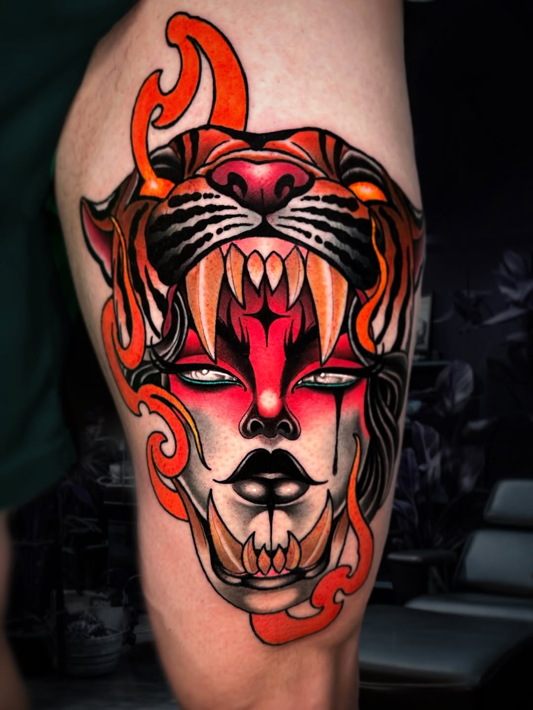 Red and orange demonic face with tiger head, flames, and skull chin tattoo on calf with bold black outlines and vibrant color work.