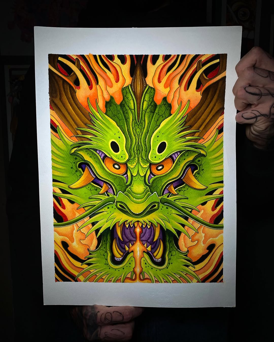 Vibrant green dragon head with orange eyes and flames, featuring purple mouth details and symmetrical design on white paper.