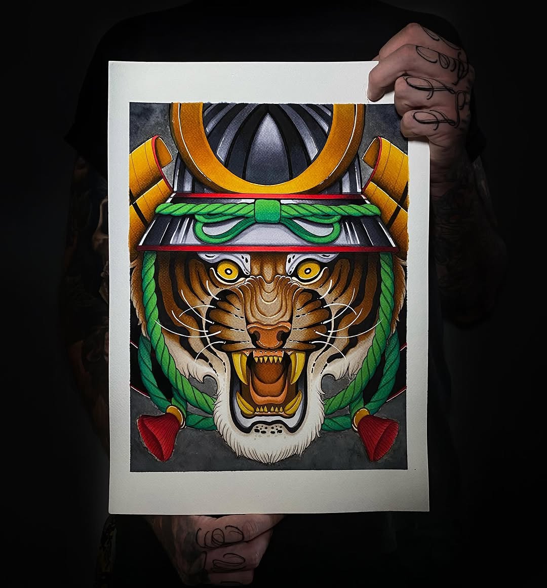 Tattooed hand holding artwork of a fierce tiger head with golden eyes, wearing an ornate helmet with gold and green decorative elements, rendered in vibrant colors.