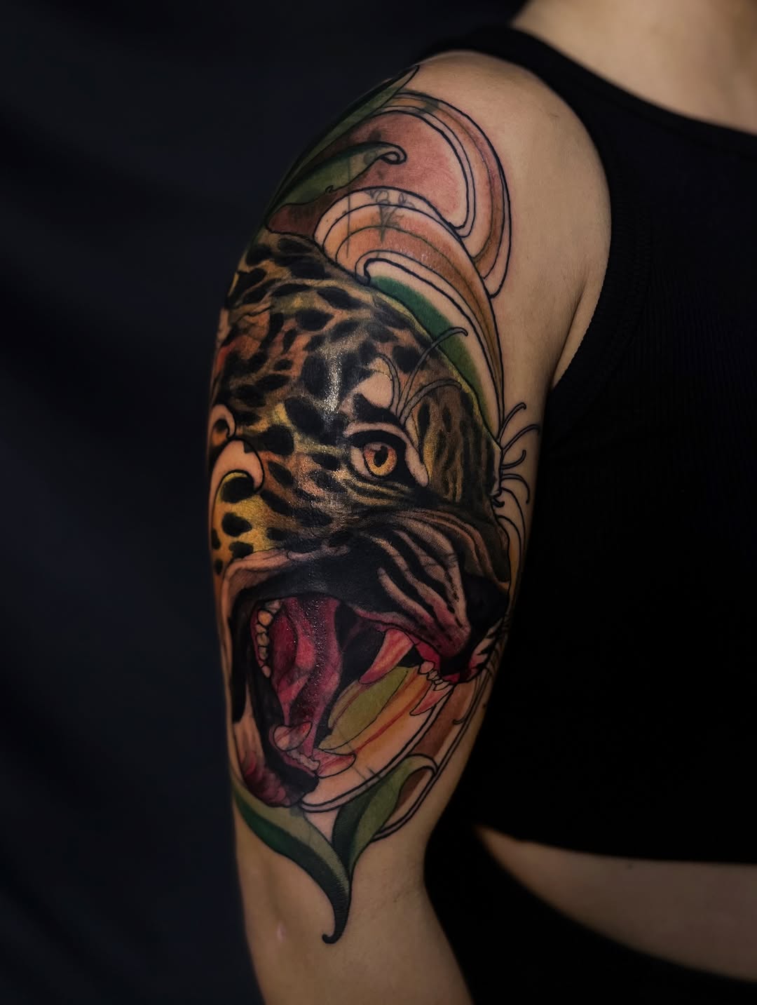 Leopard head with open mouth and decorative botanical elements in orange, green, and burgundy colors on upper arm.