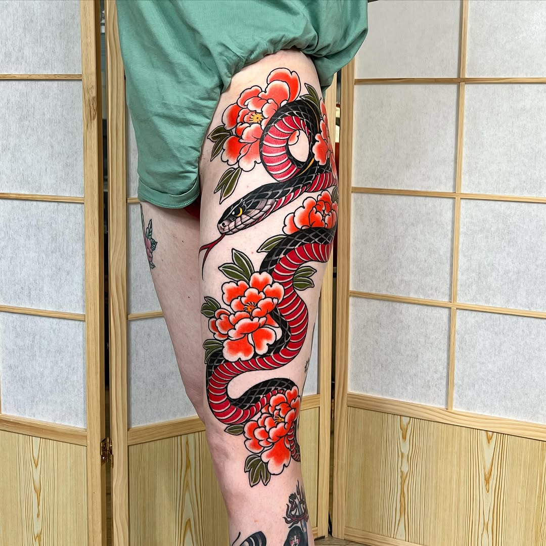 Colorful leg tattoo featuring a red snake coiled around bright red flowers with green leaves, displayed on the thigh and calf.